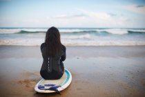 Вид сзади на серфера, сидящего на борту на пляже — стоковое фото
