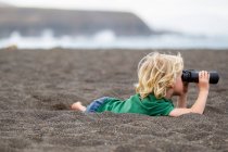 Niño usando prismáticos en la playa - foto de stock