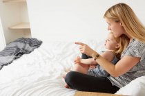 Mid adult woman sitting with toddler daughter on bed — Stock Photo