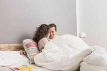 Paar liegt mit Frühstück auf Tablett im Bett — Stockfoto