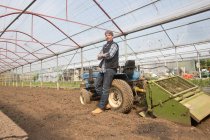Retrato de agricultor ecológico con tractor en polytunnel - foto de stock