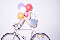 Woman sitting on bicycle hiding behind bunch of balloons — Stock Photo