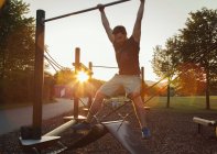 Silhouetted young man swinging on playground climbing frame at sunset — Stock Photo