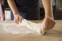 Cropped image of baker stretching bread dough — Stock Photo