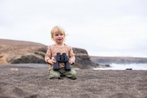 Toddler girl holding binoculars on beach — Stock Photo