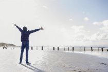 Junger Mann mit ausgebreiteten Armen am Strand stehend, brauner Sand, Purzelbaum, England — Stockfoto