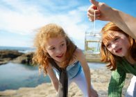 2 girls looking at fish in jar by sea — Stock Photo