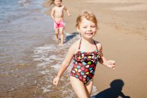 Smiling girls playing in waves on beach — Stock Photo