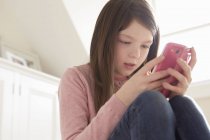 Girl sitting looking at smartphone at home — Stock Photo