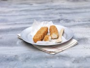 Plate of fried chunky breaded fish fingers on steel table — Stock Photo