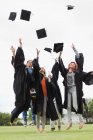 Les diplômés jetant des casquettes dans les airs — Photo de stock