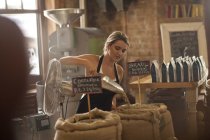 Giovane donna che lavora in caffetteria, raccogliendo caffè in sacchi — Foto stock