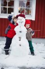 Crianças de pé com boneco de neve — Fotografia de Stock