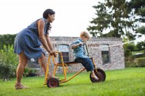 Мати штовхає сина на триколісний велосипед в саду — стокове фото