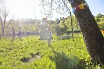 Молода жінка грає на гойдалках з друзями, що стоять на зеленому сонячному полі — стокове фото