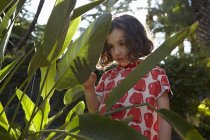 Маленькая девочка с задумчивым выражением лица стоит среди листвы — стоковое фото