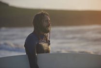 Joven surfista masculino llevando tabla de surf, Devon, Inglaterra, Reino Unido - foto de stock
