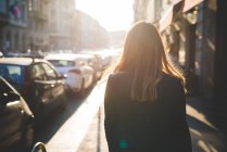 Rear view of young woman on city street in sunlight — Stock Photo