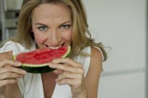 Reife Frau beißt Wassermelone und schaut in die Kamera — Stockfoto