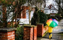 Visão traseira do menino em anorak amarelo carregando guarda-chuva ao longo da rua — Fotografia de Stock