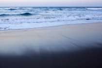 Морские волны на песчаном пляже в сумерках — стоковое фото