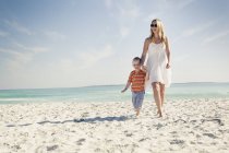 Madre e hijo paseando por la playa de arena - foto de stock