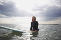 Портрет старшої жінки, що сидить на дошці для серфінгу в морі — стокове фото