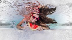 Vista subaquática da mulher usando óculos de sol, comendo fatia de melancia, sorrindo — Fotografia de Stock