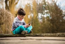 Мальчик играет на смартфоне на детской площадке — стоковое фото