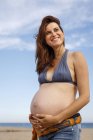 Donna incinta sulla spiaggia, mano sullo stomaco — Foto stock
