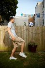 Jeune homme coups de pied football dans le jardin — Photo de stock