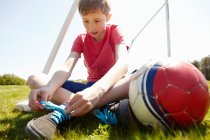 Хлопчик сидить на полі зав'язуючи взуття мереживо — стокове фото