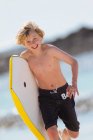 Boy carrying surfboard on beach — Stock Photo