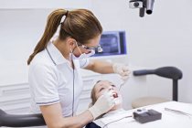 Dentista em clínica odontológica realizando exame odontológico em mulher jovem — Fotografia de Stock