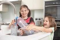 Meninas enchendo garrafa de água na cozinha — Fotografia de Stock