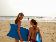 Ragazze che trasportano boogie tavole sulla spiaggia — Foto stock