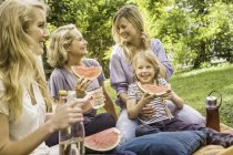 Tres generaciones de mujeres haciendo picnic con sandía - foto de stock