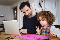 Menina desenho à mesa, enquanto o pai usando laptop — Fotografia de Stock