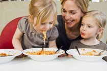 Mid adult mother eating spaghetti with two little daughters — Stock Photo