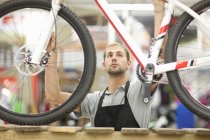 Jeune homme tenant un vélo dans un atelier de réparation — Photo de stock