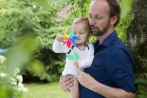 Vater und kleine Tochter spielen mit Windrad im Garten — Stockfoto