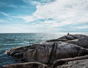 Person sitzt auf Felsformation an der Küste — Stockfoto