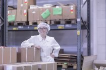 Fabrikarbeiter in Lagerhalle trägt Haarnetz und blickt lächelnd in die Kamera — Stockfoto