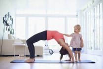 Mid adult mother practicing yoga with curious toddler daughter — Stock Photo
