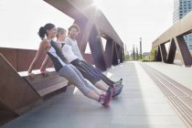 Two women and man push up training leaning against urban footbridge — Stock Photo