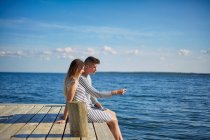 Couple sitting on wooden pier, looking at view — Stock Photo