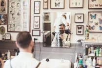 Mittlerer erwachsener Mann justiert Krawatte, während er in Friseurladen-Spiegel schaut — Stockfoto