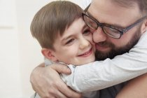 Hombre adulto medio e hijo abrazándose entre sí - foto de stock