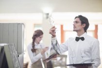 Camarero sosteniendo y comprobando copa de vino en restaurante - foto de stock