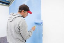 Vista trasera del hombre pintando la pared azul - foto de stock